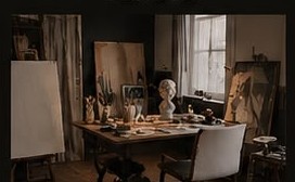 Warm artist studio with an easel, a working desk of objects and brushes, chairs and a classical bust in natural window light